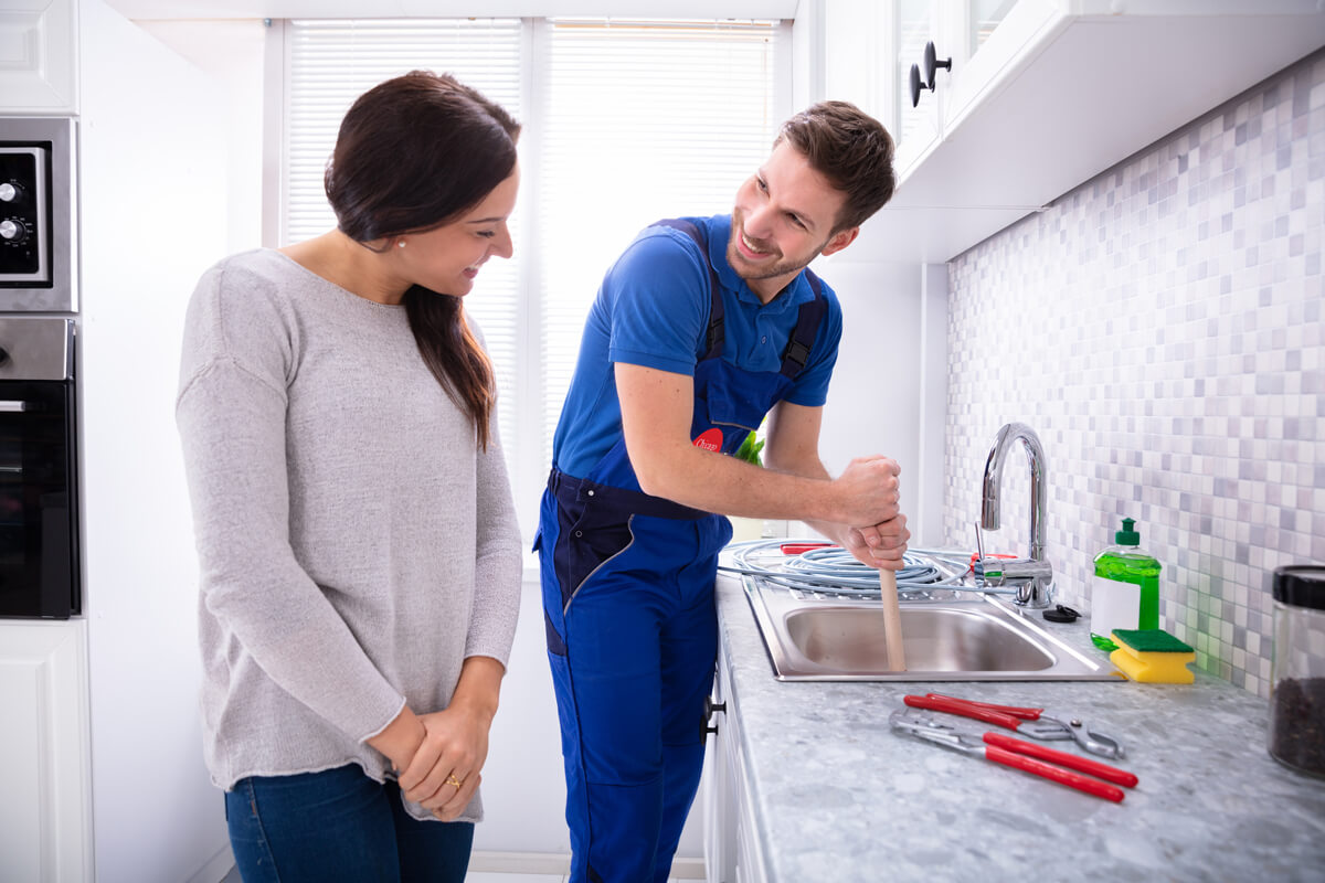 Happy Woman Looking at Male Plumber using Plunger